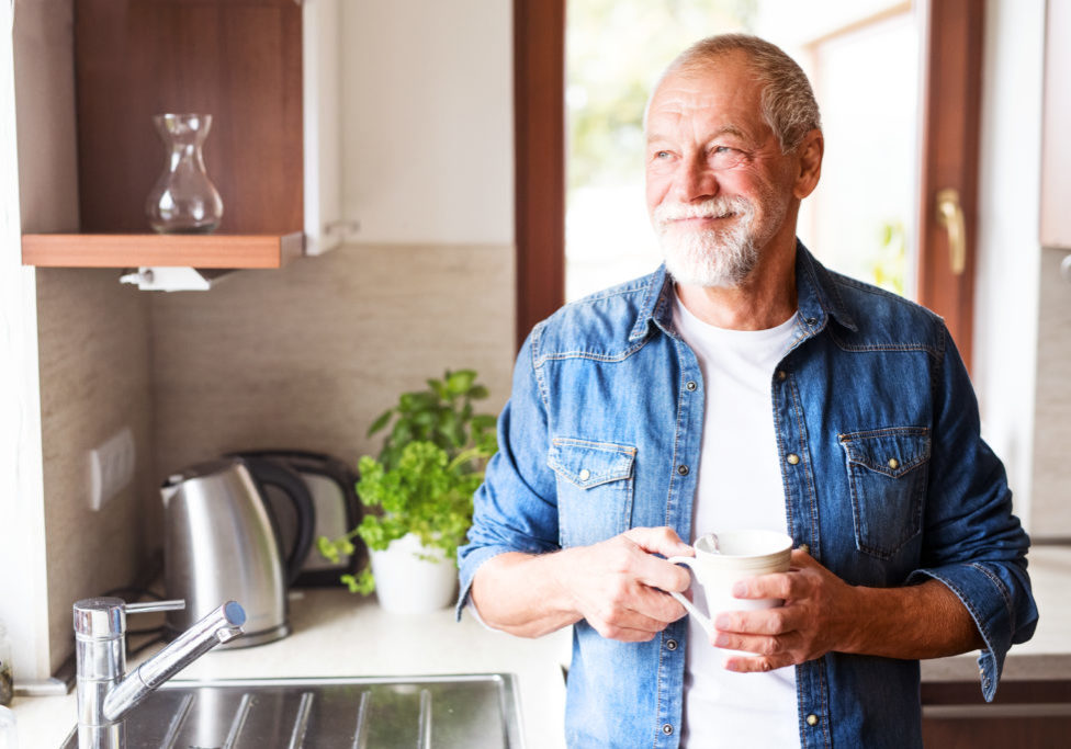 Happy senior man in the kitchen. An old man inside the house, holding a cup of coffee.