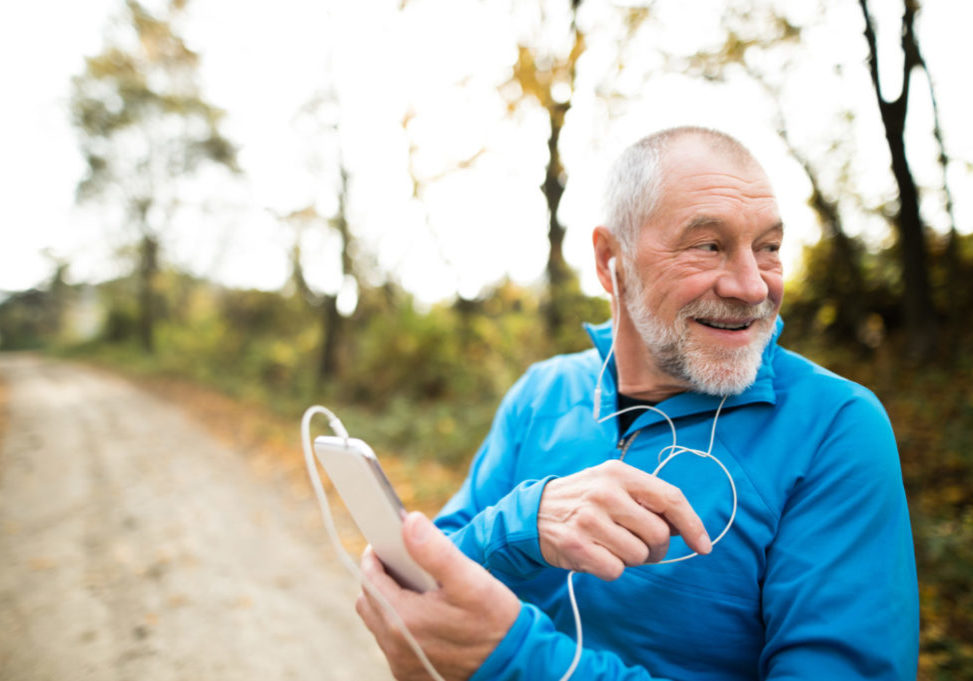 Senior runner in nature. Man with smart phone with earphones. Listening music or using a fitness app. Using phone app for tracking weight loss progress, running goal or summary of his run.